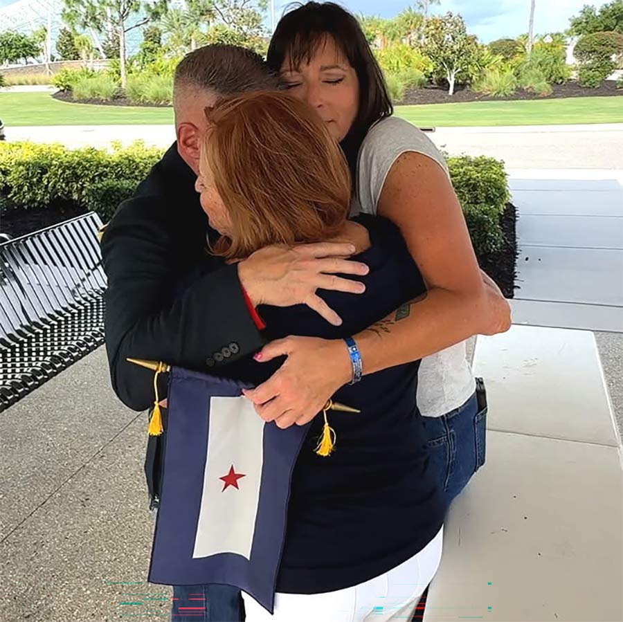 Three people embrace outdoors while one holds a Red Star Service Banner with a single red star